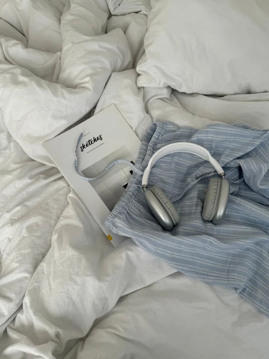 Over-ear headphones resting on soft bedding beside a book
